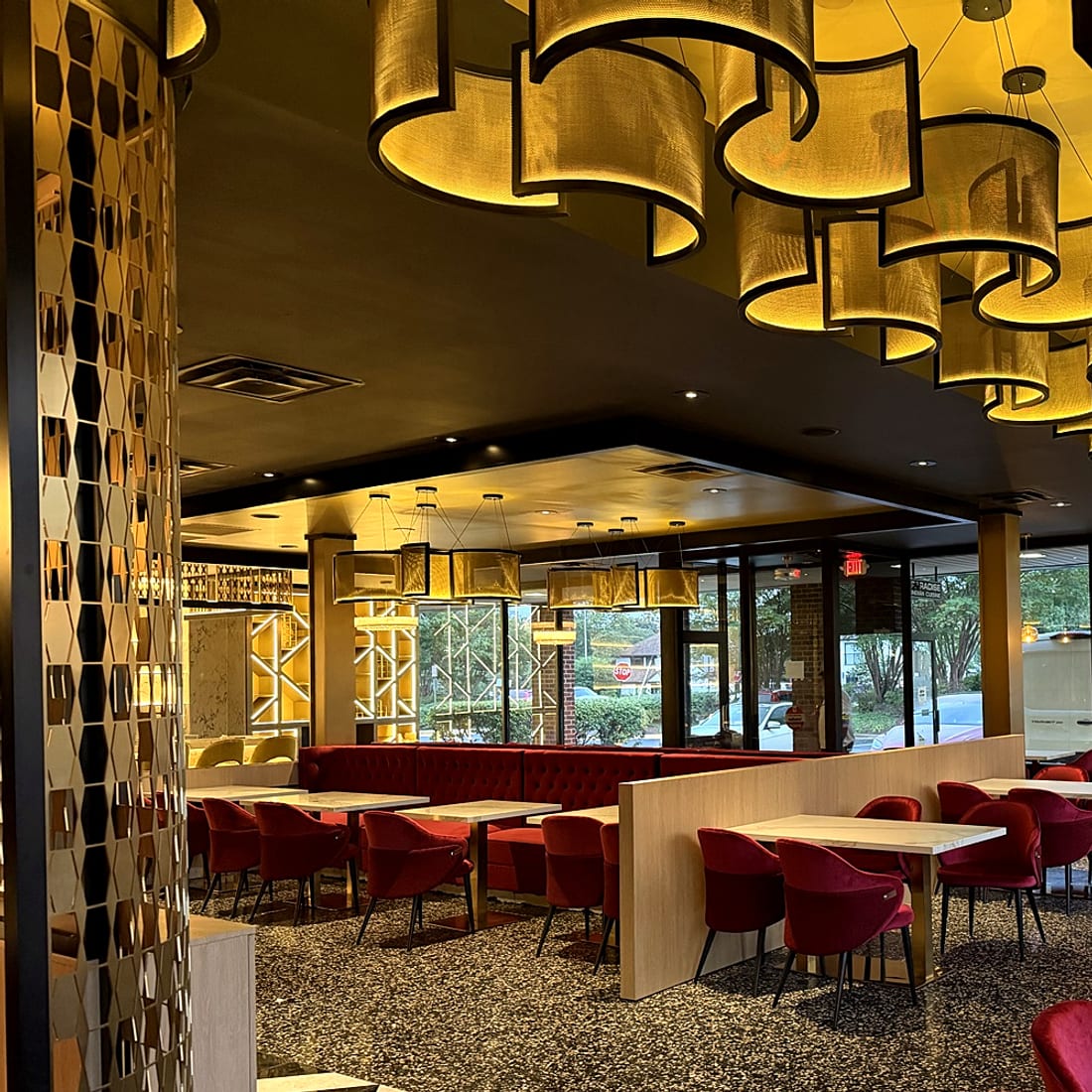 Brass mosaic column with gold ribbon chandelier and red banquettes beyond